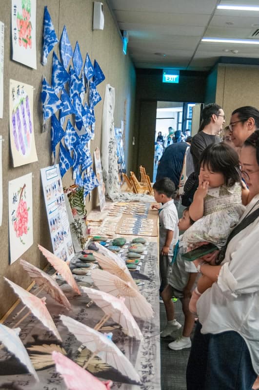 Families viewing K1 and K2 Chinese cultural artwork, including calligraphy and paper crafts